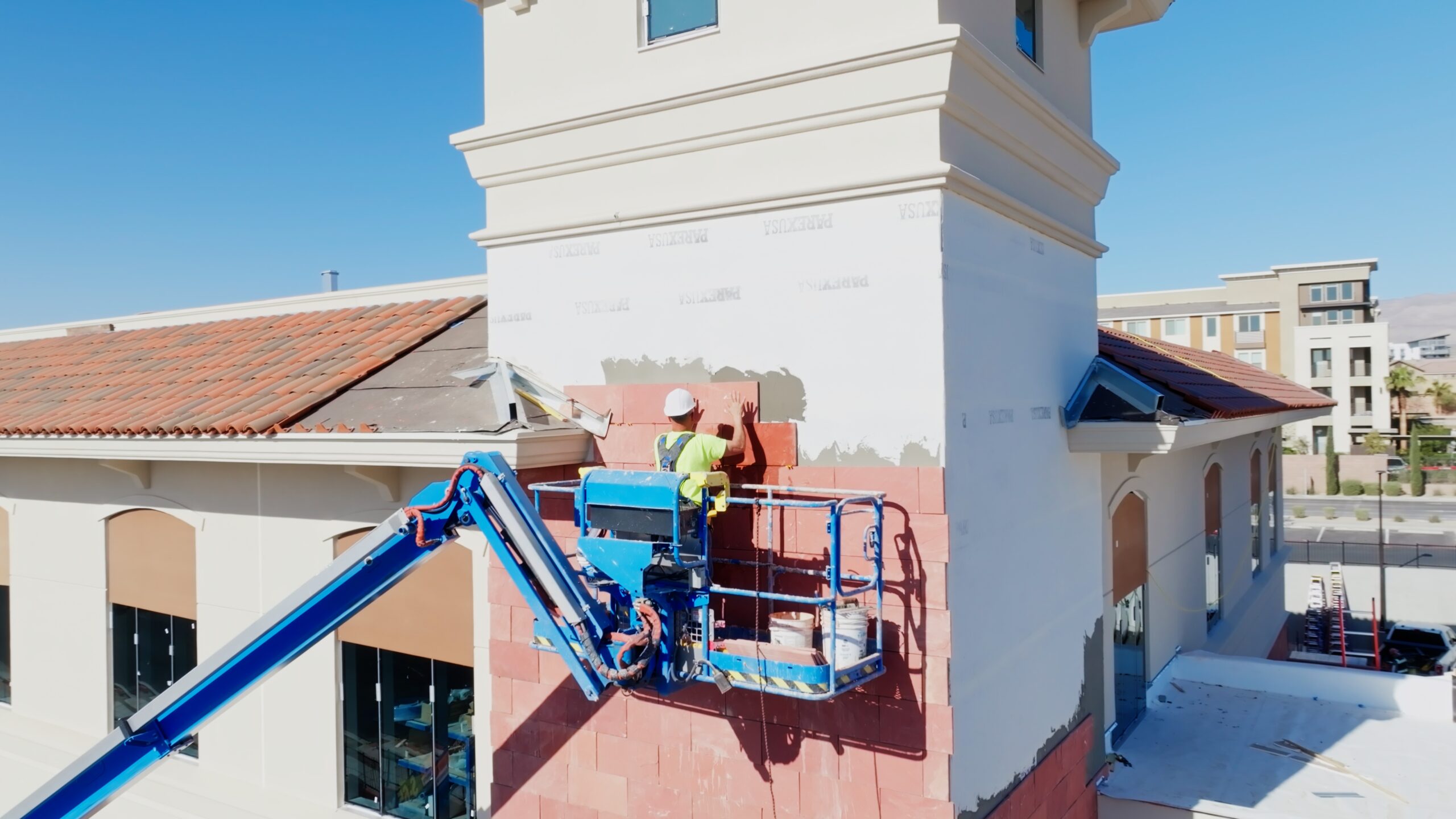 Construction worker on a hydraulic lift installing exterior tile on a large building tower.