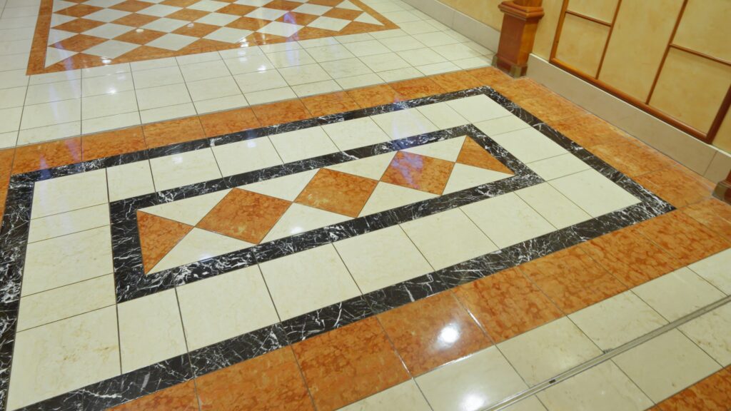 Intricate patterned floor tiling with a decorative border featuring white, orange, and black tiles, highlighting custom flooring designs.