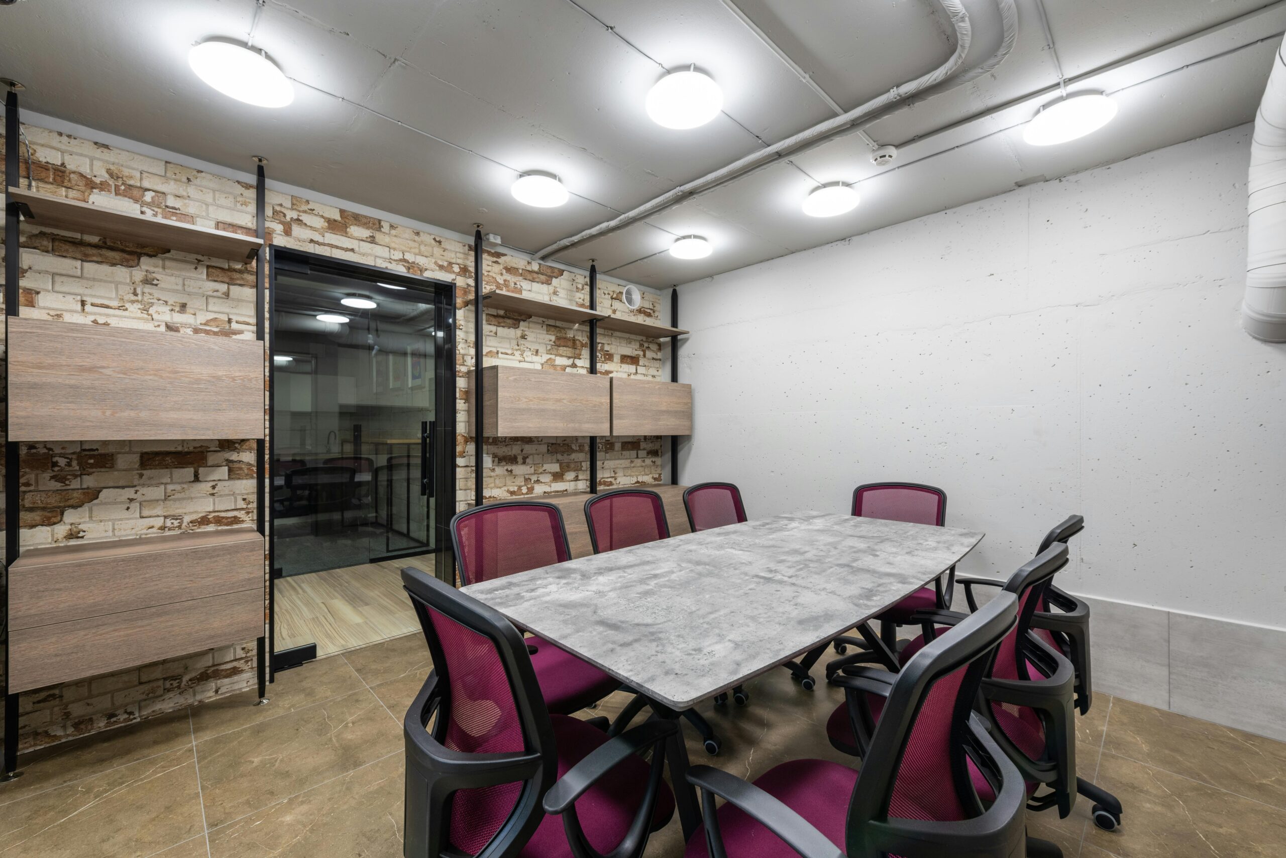 Contemporary meeting room with sleek dark tile flooring and a long conference table, set against walls with exposed textures.
