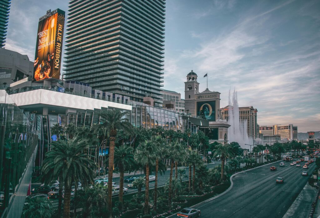 Overview of the Las Vegas Strip featuring the Cosmopolitan and Bellagio hotels, with palm trees and cars on the boulevard.